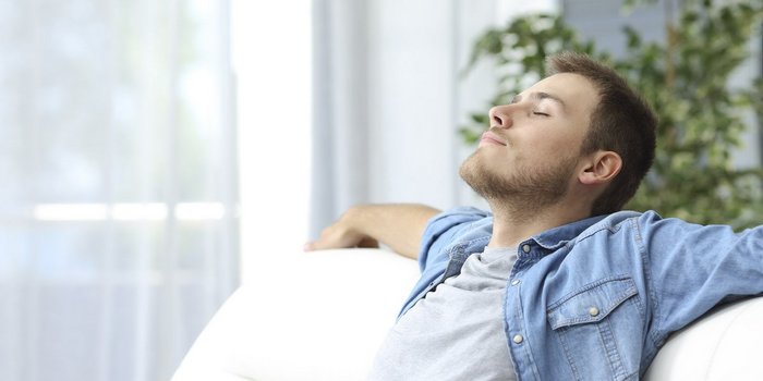 Ein Mann sitzt zufrieden auf dem Sofa und er hat die Arme auf der Rücklehne ausgestreckt. der Mann hat die Augen sind geschloßen.