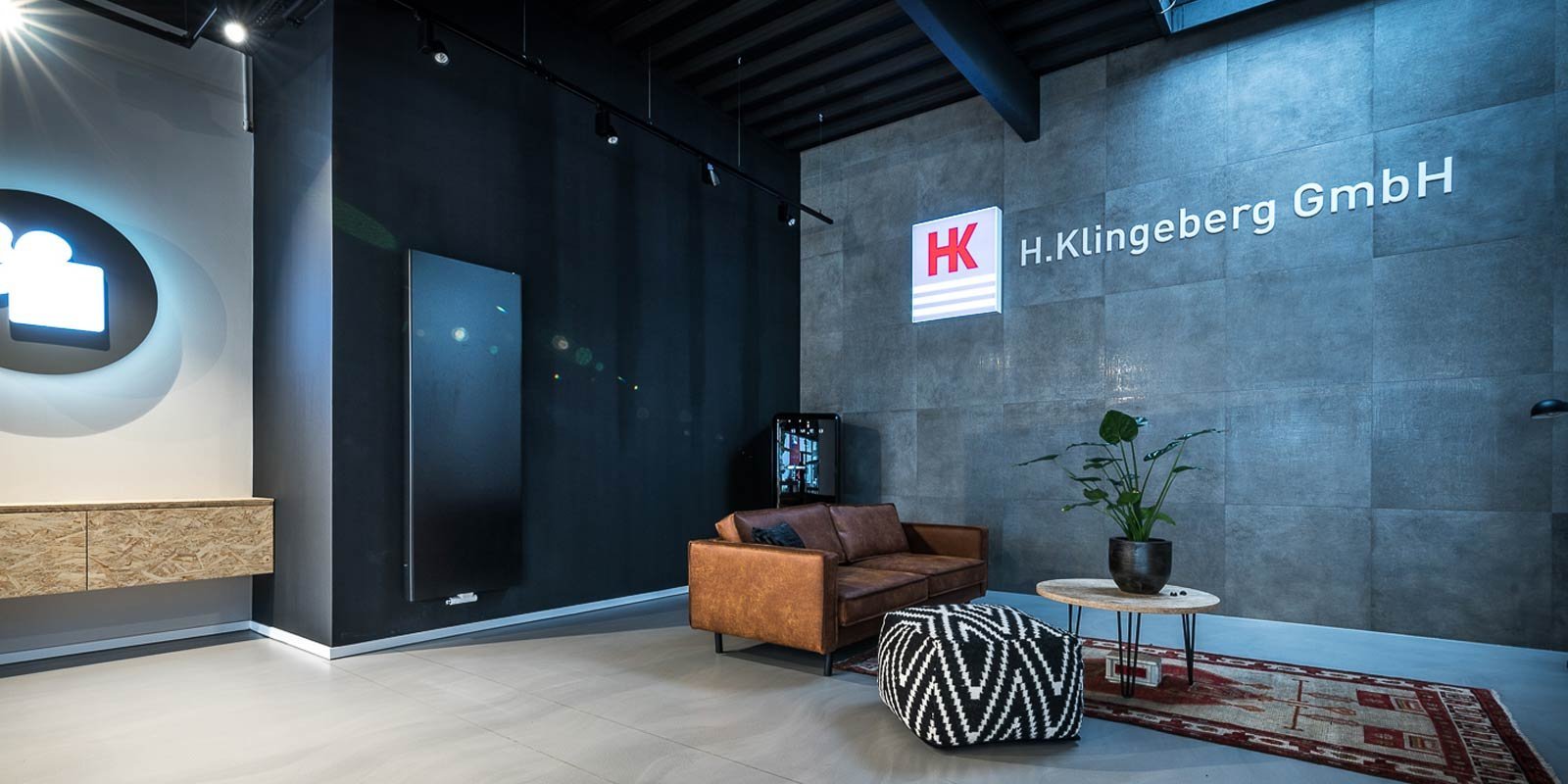 Ein modernes Büro mit einem braunen Ledersofa, einem runden Tisch und einer Pflanze auf einem minimalistischen Teppich.