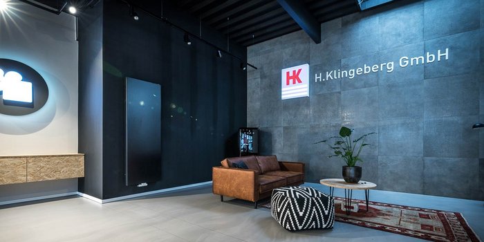 Ein modernes Büro mit einem braunen Ledersofa, einem runden Tisch und einer Pflanze auf einem minimalistischen Teppich.