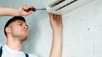 Ein Mechatroniker der an einer Klimaanlage schraubt