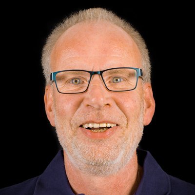 Ein älterer Mann mit Brille lächelt freundlich in die Kamera, sein graues Haar und Bart verleihen ihm einen warmen Ausdruck.