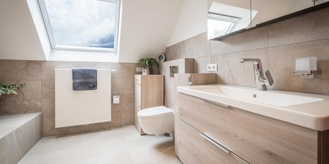 Ein modernes Badezimmer mit einem großen Fenster, das Tageslicht hereinlässt, und eleganten Holz- und Fliesenoberflächen.