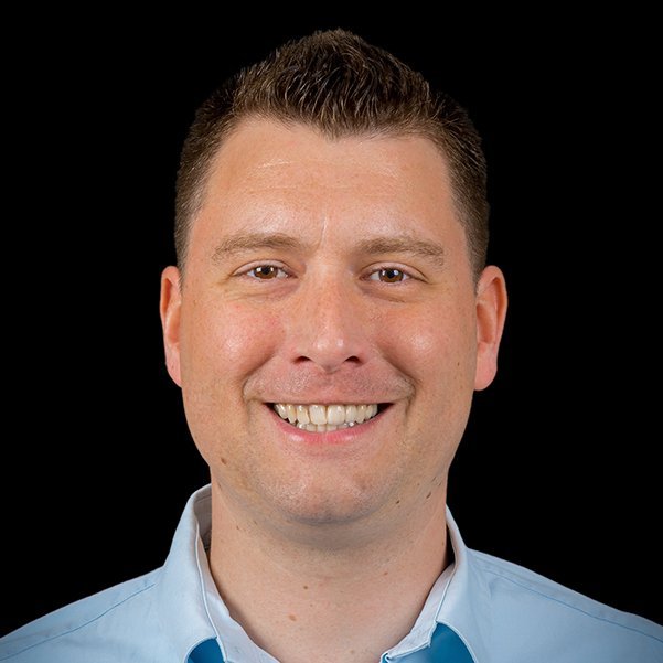 Der Mann hat ein breites Lächeln und zeigt freundliche Gesichtszüge, während er direkt in die Kamera schaut.