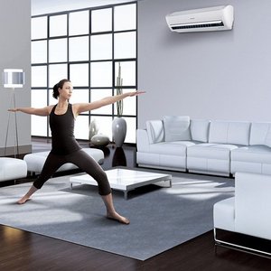 Eine Frau in sportlicher Kleidung führt eine Yoga-Übung in einem modernen Wohnzimmer mit großen Fenstern aus.