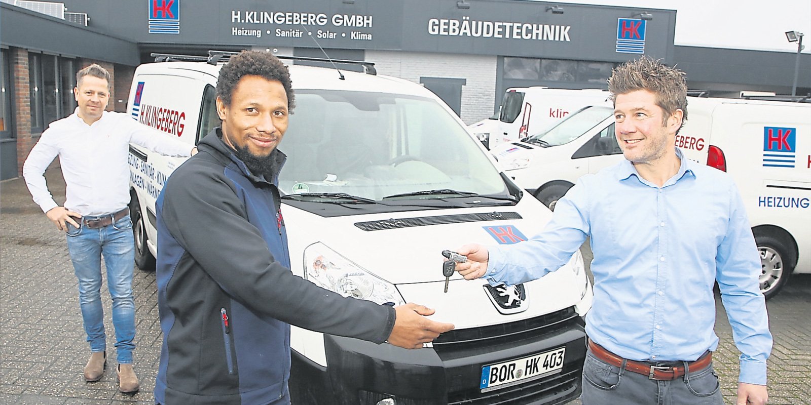 Zwei Männer stehen vor einem Lieferwagen, einer von ihnen lächelt, während er die Schlüssel überreicht, der andere nimmt sie entgegen.