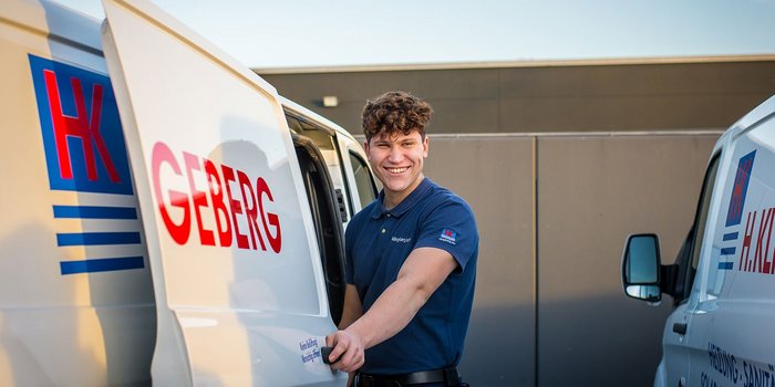 Ein junger Mann mit lockigem Haar lächelt, während er die Tür eines Lieferwagens öffnet, der mit 'HK GEBERG' beschriftet ist.