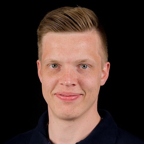 Der Mann hat eine helle Hautfarbe und trägt ein dunkles Oberteil, während er direkt in die Kamera schaut.