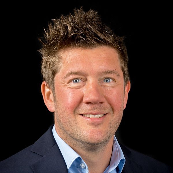 Der Mann hat ein freundliches Lächeln und strahlend blaue Augen, während er in die Kamera schaut.