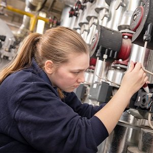 Eine junge Frau arbeitet konzentriert an einer technischen Maschine, während sie Kabel anschließt und Einstellungen vornimmt.
