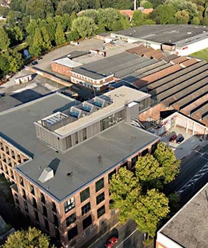 Eine Luftaufnahme eines modernen Gebäudes mit einem flachen Dach und großen Fenstern, umgeben von Bäumen und anderen Industriegebäuden.