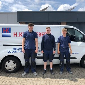 Drei junge Handwerker stehen lächelnd vor einem Firmenfahrzeug, das mit dem Logo und den Dienstleistungen der Firma beschriftet ist.