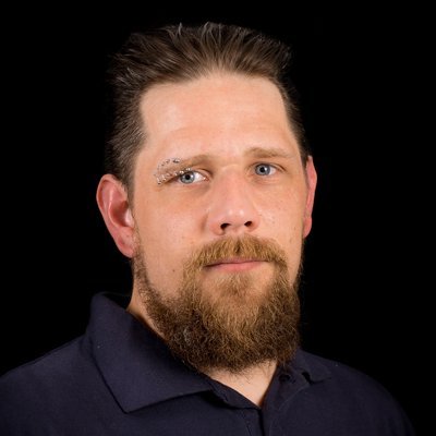 Ein Mann mit einem dichten Bart und einem auffälligen Augenbrauenpiercing blickt direkt in die Kamera.