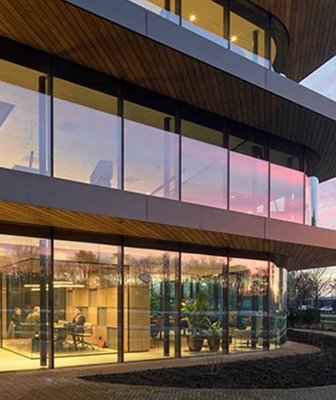 Ein modernes Bürogebäude mit großen Fenstern, das bei Sonnenuntergang beleuchtet ist, zeigt eine Besprechung im Inneren.