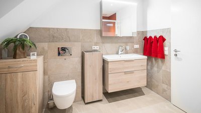 Ein modernes Badezimmer mit hellen Fliesen, einem Holzwaschtisch und roten Handtüchern, die an der Wand hängen.