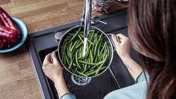 Eine Frau haelt ein Topf mit Bohnen unter der laufenden Kuechenspuehle