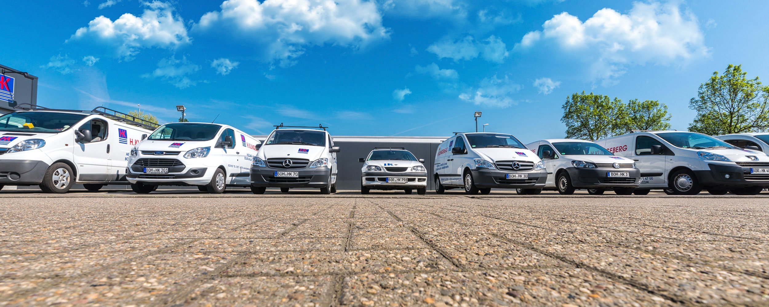 Eine Reihe von Lieferwagen steht auf einem Parkplatz unter einem strahlend blauen Himmel mit wenigen Wolken.