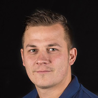Ein junger Mann mit kurzen, dunklen Haaren und einem neutralen Gesichtsausdruck blickt direkt in die Kamera.