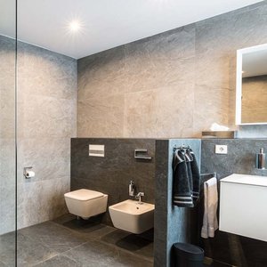 Ein modernes Badezimmer mit grauen Fliesen, einer Dusche und einem weißen Waschbecken, das stilvoll und minimalistisch wirkt.
