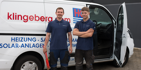 Zwei Handwerker stehen lächelnd vor einem weißen Lieferwagen, der mit dem Firmennamen und Dienstleistungen beschriftet ist.