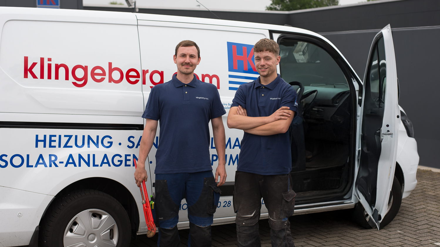 Zwei Handwerker stehen lächelnd vor einem weißen Lieferwagen, der mit dem Firmennamen und Dienstleistungen beschriftet ist.
