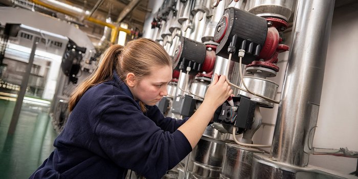 Eine junge Frau arbeitet konzentriert an einer technischen Vorrichtung in einer industriellen Umgebung.