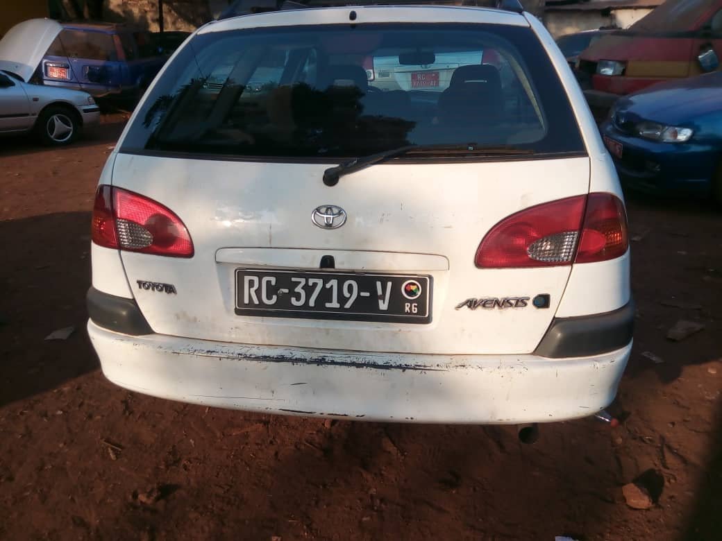 Die Rückansicht eines weißen Toyota Avensis zeigt eine beschädigte Stoßstange und ein Nummernschild mit der Aufschrift RC-3719-V.