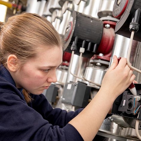 Eine junge Frau arbeitet konzentriert an einer technischen Anlage, während sie Kabel und Geräte überprüft.