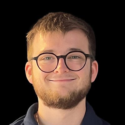 Ein junger Mann mit Brille lächelt freundlich in die Kamera, sein Bart und die Frisur sind gepflegt.