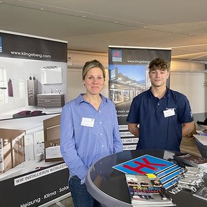 Ein Mann und eine Frau stehen an einem Messestand, umgeben von Werbematerialien für Sanitär- und Heizungsinstallationen.