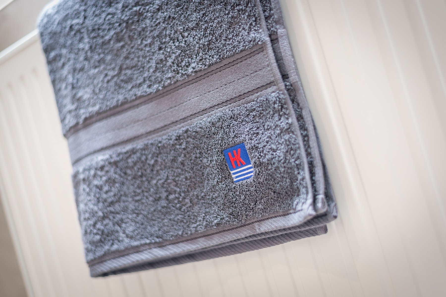 Ein graues Handtuch hängt ordentlich an einem Heizkörper, mit einem auffälligen Logo in Blau und Rot.