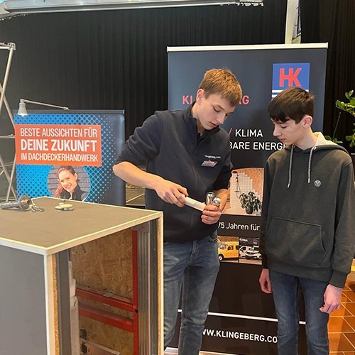 Ein junger Mann zeigt einem anderen, wie man eine Lampe in eine Halterung einsetzt, während sie in einem Ausstellungsraum stehen.