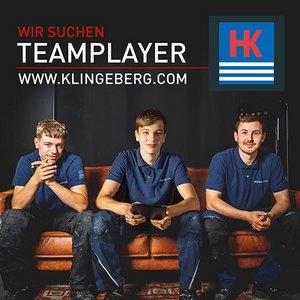 Drei junge Handwerker sitzen auf einer Couch, lächeln und halten ein Tablet, während sie nach Teamplayern suchen.