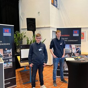Zwei junge Männer stehen an einem Messestand, umgeben von Informationsmaterialien über erneuerbare Energien.