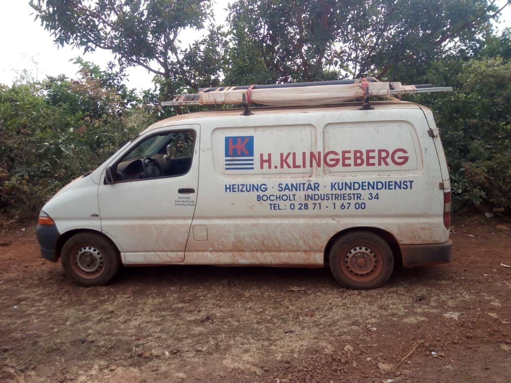 Ein weißer Lieferwagen mit dem Logo von H. Klingeberg steht auf einem unbefestigten Weg, umgeben von Bäumen und Sträuchern.