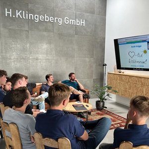 Eine Gruppe von Jugendlichen sitzt in einem modernen Raum und schaut auf einen Bildschirm mit einer herzlichen Willkommensnachricht.